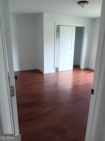 a view of an empty room with wooden floor and a bathroom