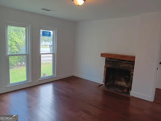 an empty room with wooden floor fireplace and windows