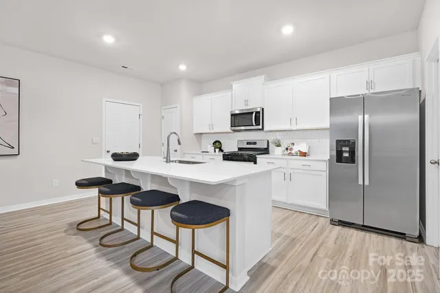 a kitchen with stainless steel appliances a refrigerator a stove a sink dishwasher and white cabinets with wooden floor