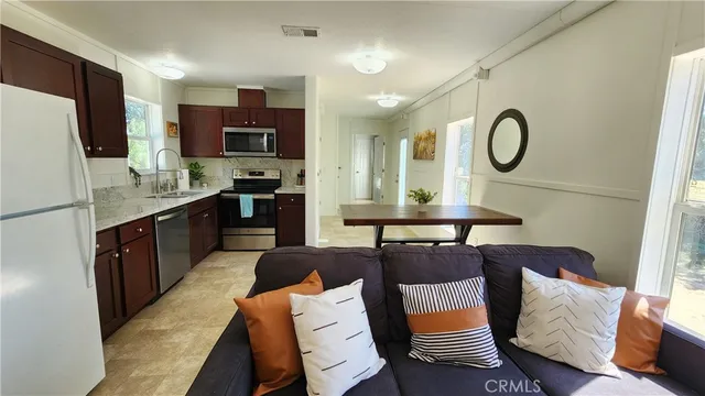 a living room with stainless steel appliances furniture a rug and a kitchen view