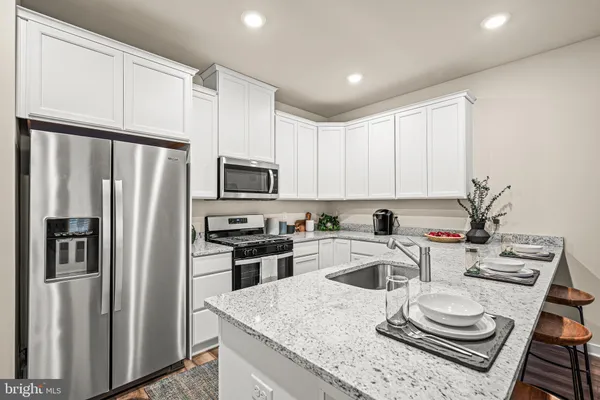 a kitchen with stainless steel appliances kitchen island granite countertop a refrigerator a sink a stove and white cabinets