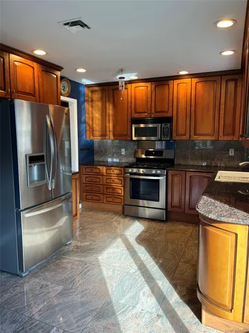 a kitchen with stainless steel appliances granite countertop a refrigerator a stove and a sink with wooden cabinets