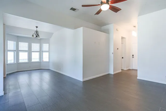 an empty room with wooden floor chandelier fan and windows