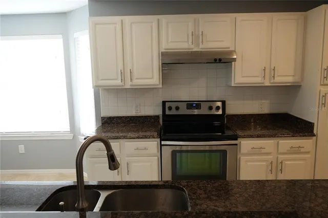 a kitchen with granite countertop a stove a sink and white cabinets