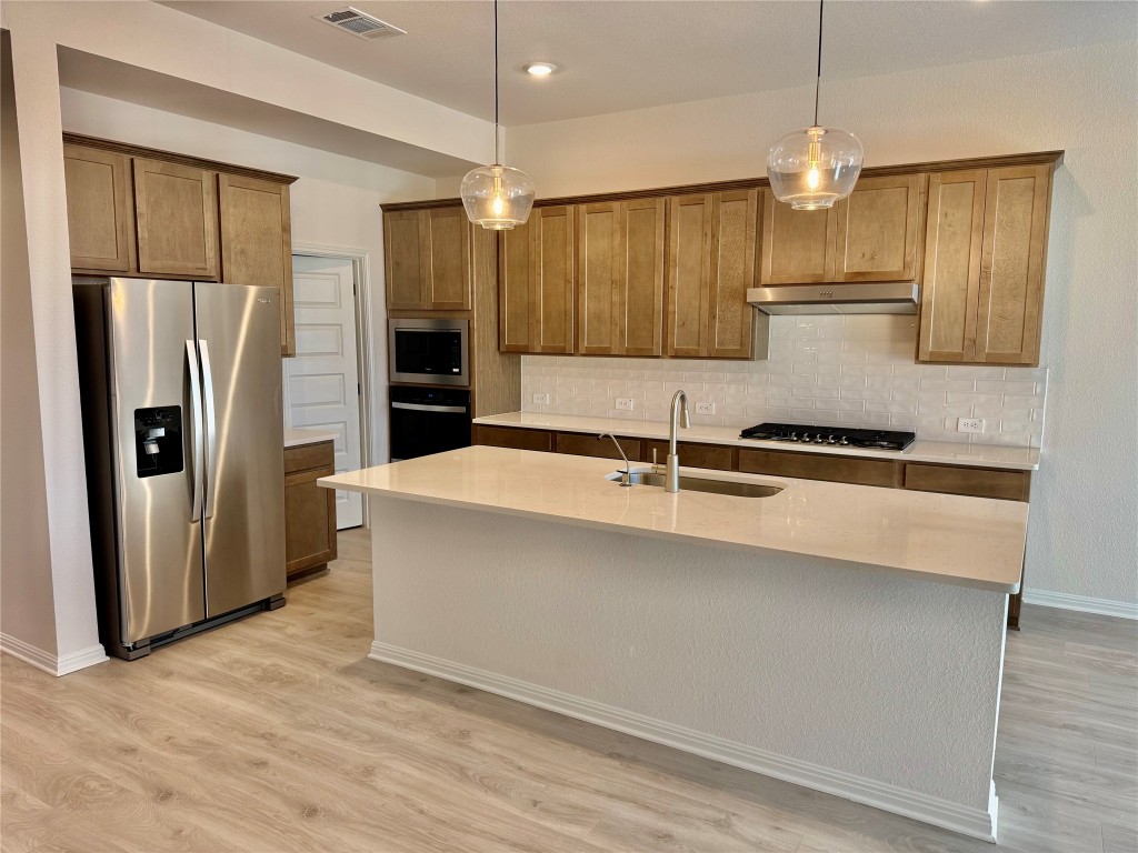 1788 South Main Street Kyle, TX 78640 - Photo 2 of 7 Kitchen featuring black appliances, hanging light fixtures, an island with sink, brown cabinetry, and backsplash