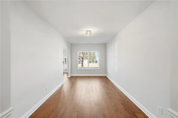 a view of empty room with wooden floor and kitchen