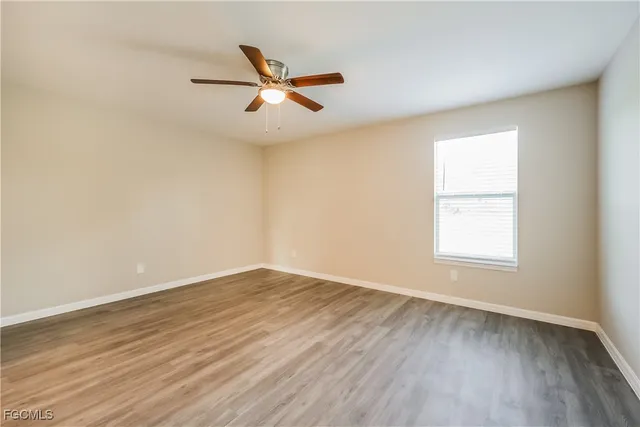 an empty room with wooden floor fan and windows