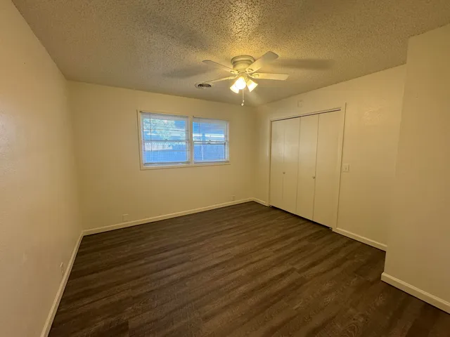 a view of an empty room with wooden floor and a fan
