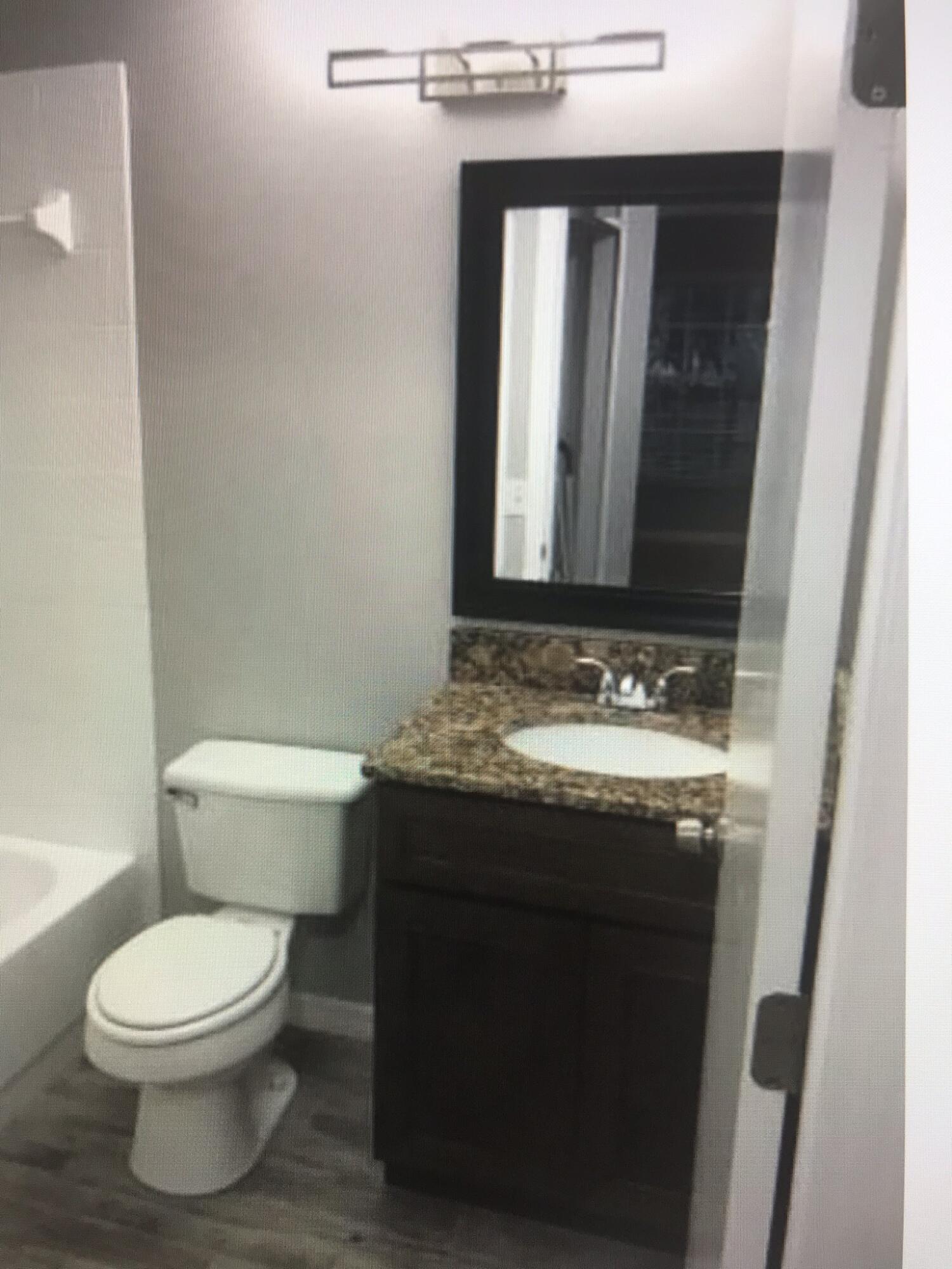 2836 Osprey Cove Place, Unit 201 Kissimmee, FL 34746 - Photo 4 of 11 a bathroom with a granite countertop toilet a sink and a mirror