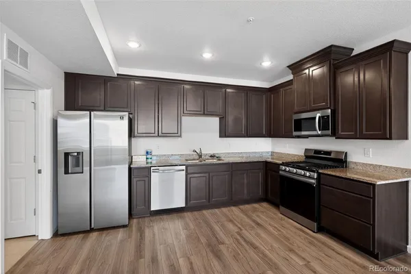 a kitchen with stainless steel appliances granite countertop wooden cabinets a refrigerator a sink a stove a microwave and wooden floors