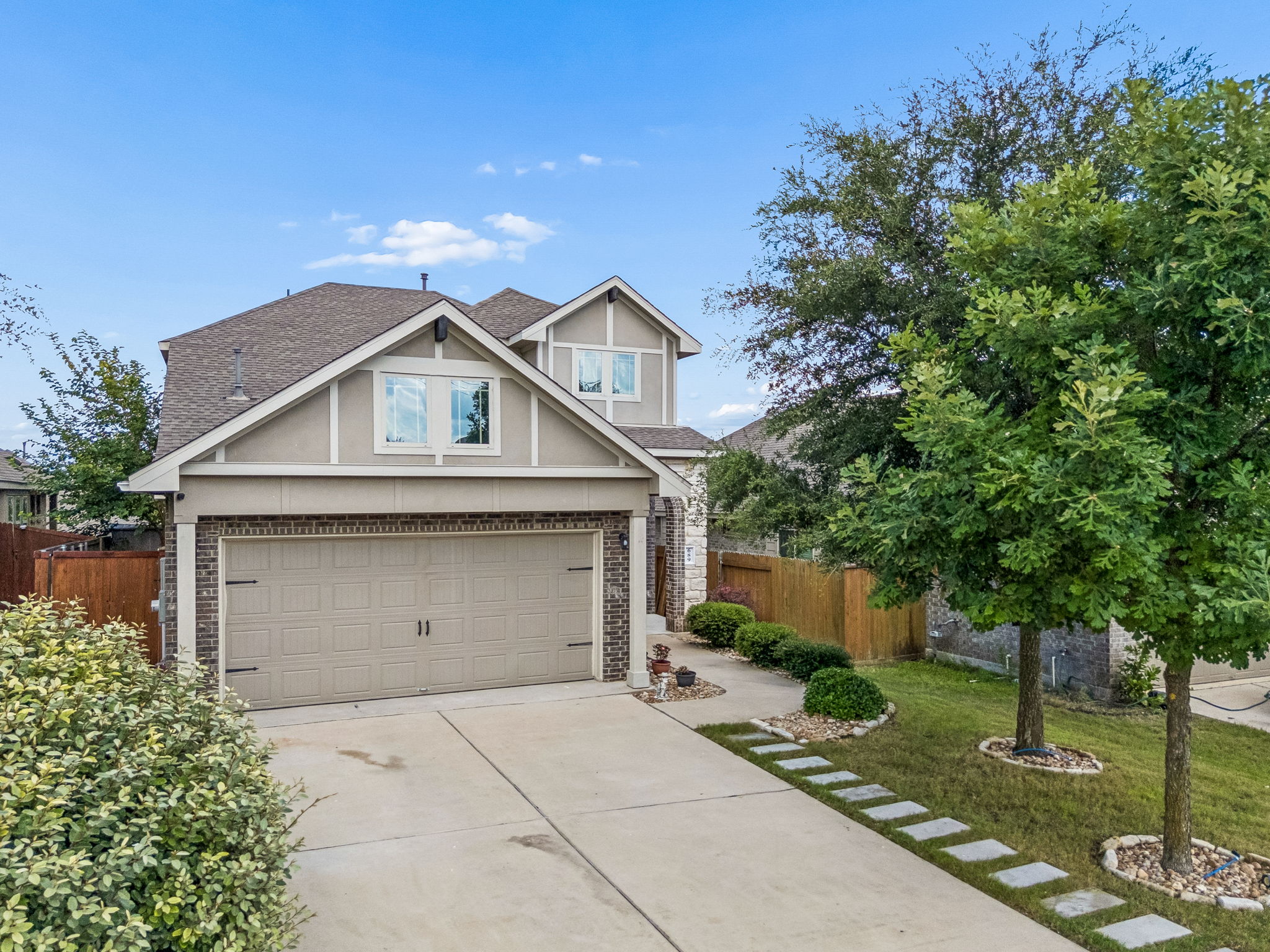 A welcoming facade showcases mature trees and a well-maintained driveway leading to a two-car garage.