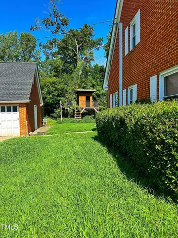 a view of a brick house with a big yard plants and large trees