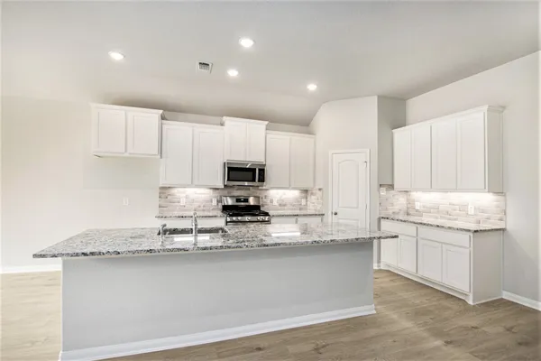 a kitchen with kitchen island granite countertop a sink a stove a counter space and cabinets