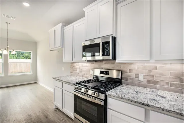 a kitchen with stainless steel appliances granite countertop white cabinets and a stove top oven