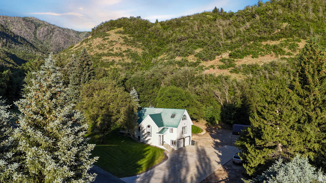 10686 South Covered Brg Cyn Road, Unit 14 Spanish Fork, UT 84660 - Photo 8 of 44 White multi-level residence with a green roof, integrated garage, and arched windows, surrounded by mature trees and verdant mountain terrain