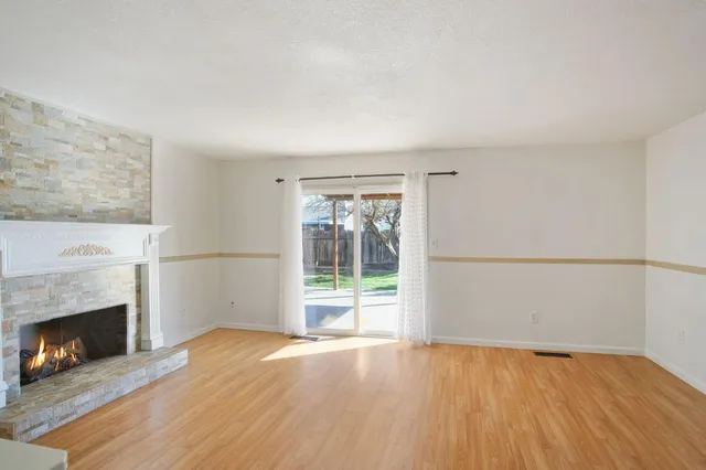 an empty room with wooden floor fireplace and windows