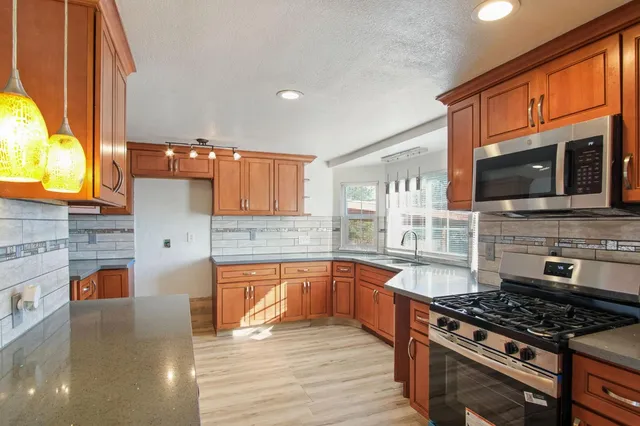 a kitchen with stainless steel appliances granite countertop a stove top oven a sink dishwasher a dining table and chairs with wooden floor