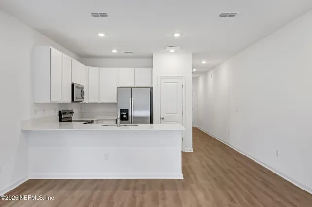 a large kitchen with stainless steel appliances granite countertop a stove a sink a refrigerator and white cabinets with wooden floor