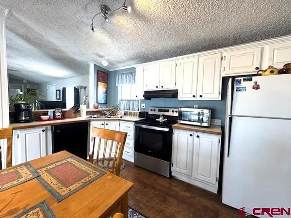 a kitchen with stainless steel appliances granite countertop a refrigerator a sink dishwasher a stove and white countertops with wooden floor