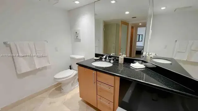 a bathroom with a granite countertop sink a toilet a mirror and vanity