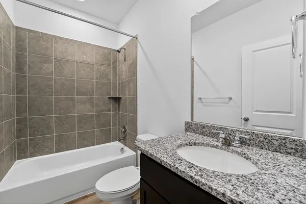 a bathroom with a granite countertop bathtub sink vanity mirror and toilet