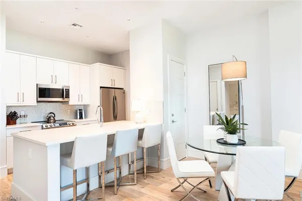 a kitchen with stainless steel appliances a dining table chairs refrigerator and sink