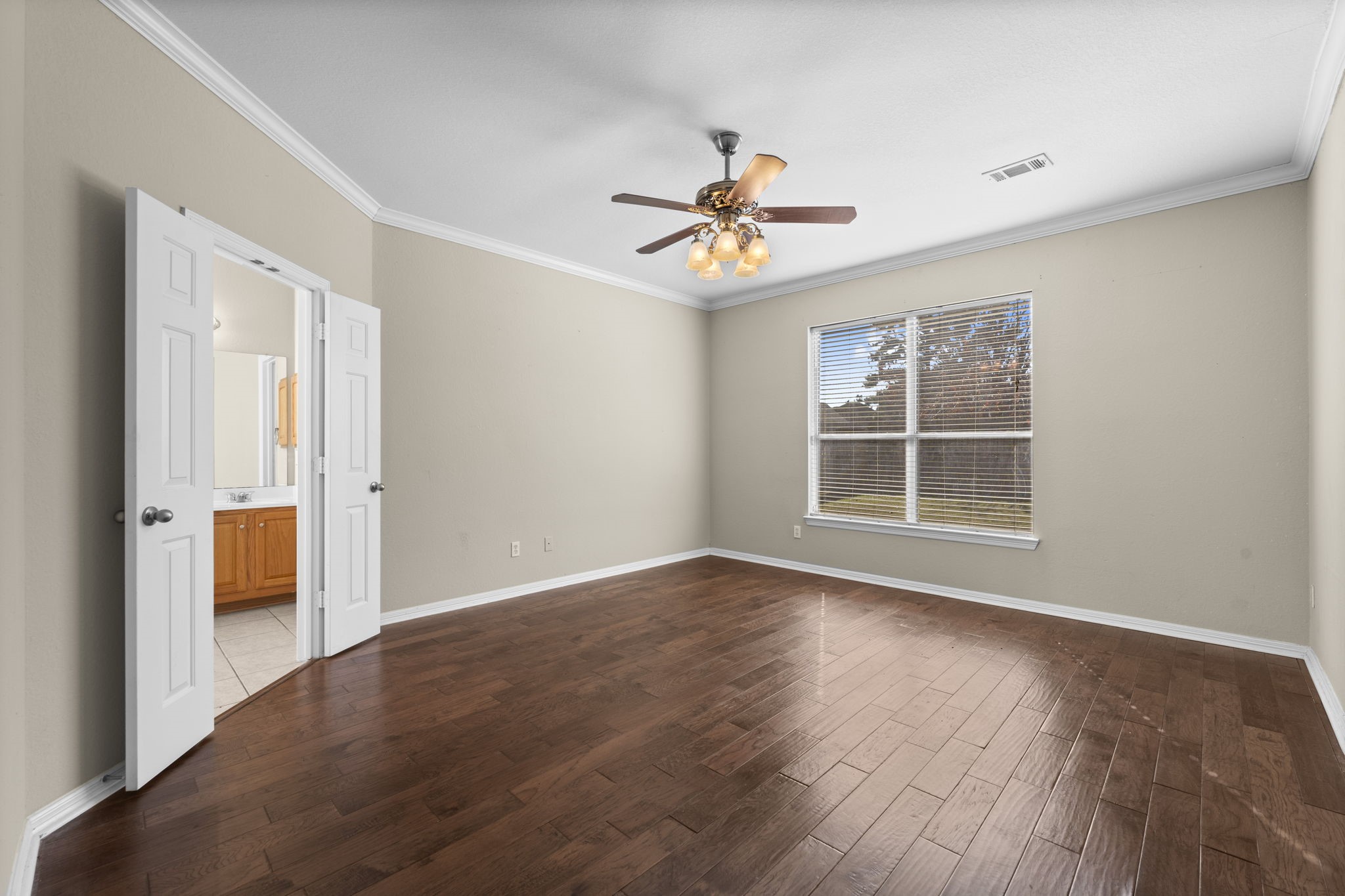 19327 Dickson Park Drive Spring, TX 77373 - Photo 16 of 43 The inviting Owner’s Suite is a private retreat designed for ultimate relaxation. A large double window fills the space with natural light and offers serene views of the backyard. Crown molding adds architectural elegance, while wood laminate flooring and a stylish ceiling fan with light complete the refined look. Spacious, serene, and beautifully appointed — the perfect escape at the end of the day.