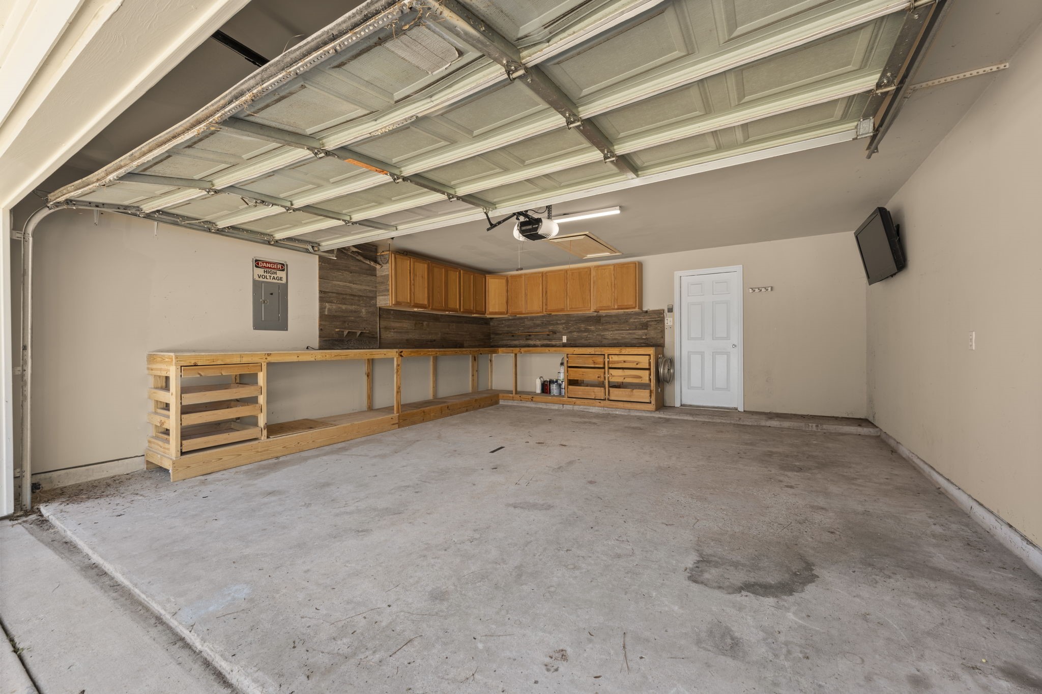 19327 Dickson Park Drive Spring, TX 77373 - Photo 34 of 43 Spacious garage featuring an L-shaped workbench with built-in shelving, cabinets, and drawer storage—ideal for projects and organization. Mounted TV adds convenience and entertainment while you work.