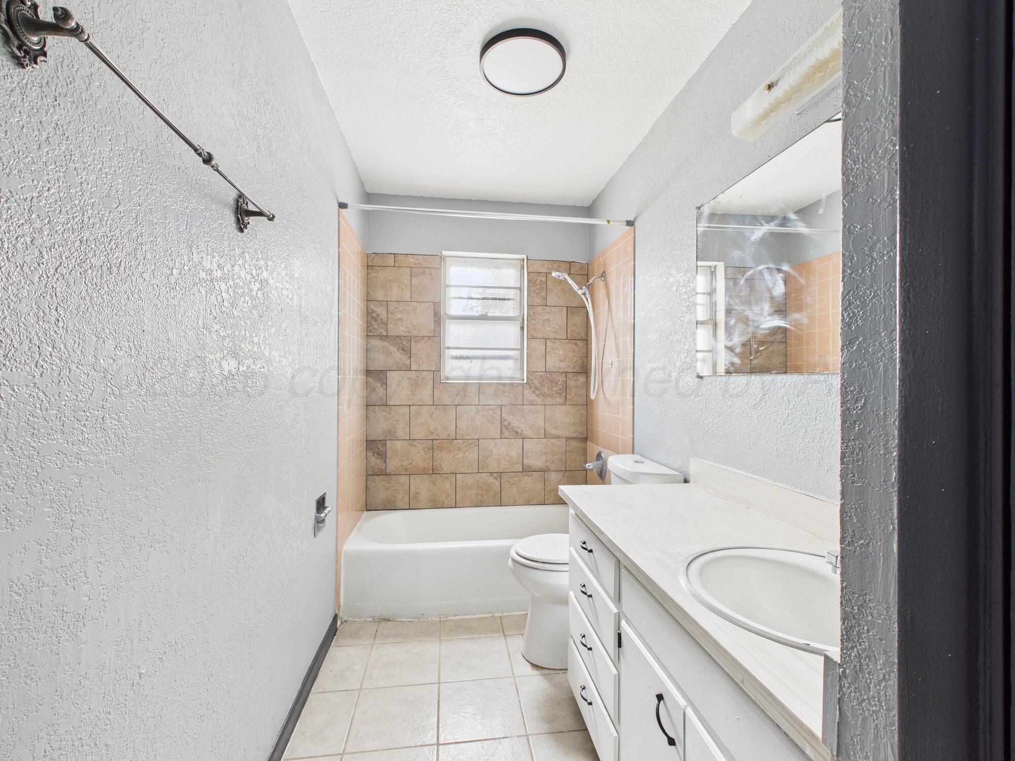 1002 Northeast 4th Street Dumas, TX 79029 - Photo 5 of 8 a bathroom with a granite countertop sink a toilet and bathtub