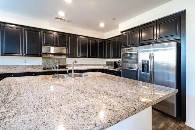 a kitchen with stainless steel appliances granite countertop a refrigerator a stove and a sink with wooden cabinets