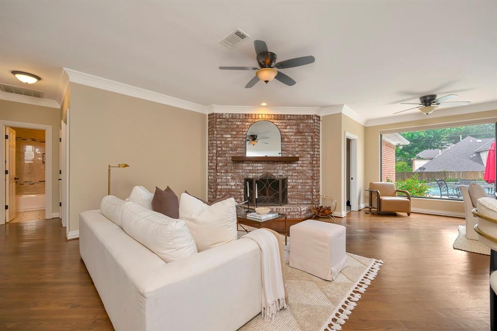 4008 Ramsgate Court Colleyville, TX 76034 - Photo 11 of 33 Spacious living area featuring wood-finish flooring, an exposed brick fireplace with a wood mantle, crown molding, and a large window overlooking the exterior