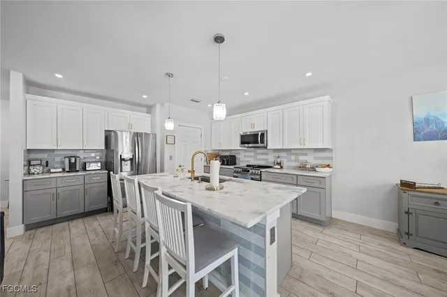 a kitchen with stainless steel appliances a stove a sink a refrigerator white cabinets and couches with wooden floor