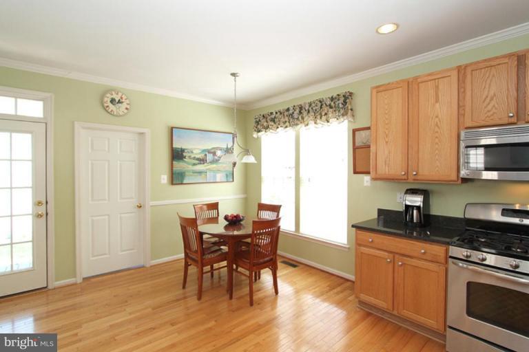 18409 Cornflower Road Boyds, MD 20841 - Photo 6 of 24 a kitchen with stainless steel appliances granite countertop a stove a refrigerator a sink a dining table and chairs with wooden floor