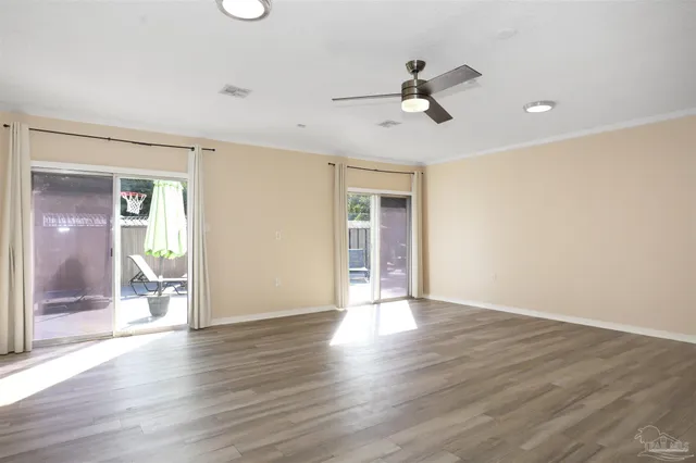 a view of an empty room with wooden floor and a ceiling fan