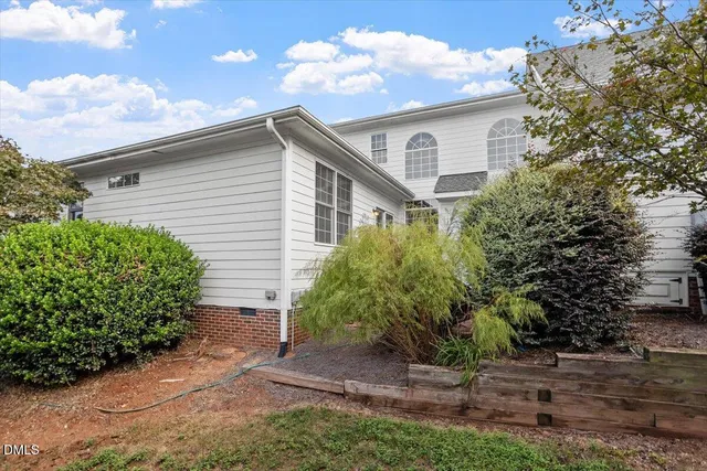 a white house with a small yard plants and large tree