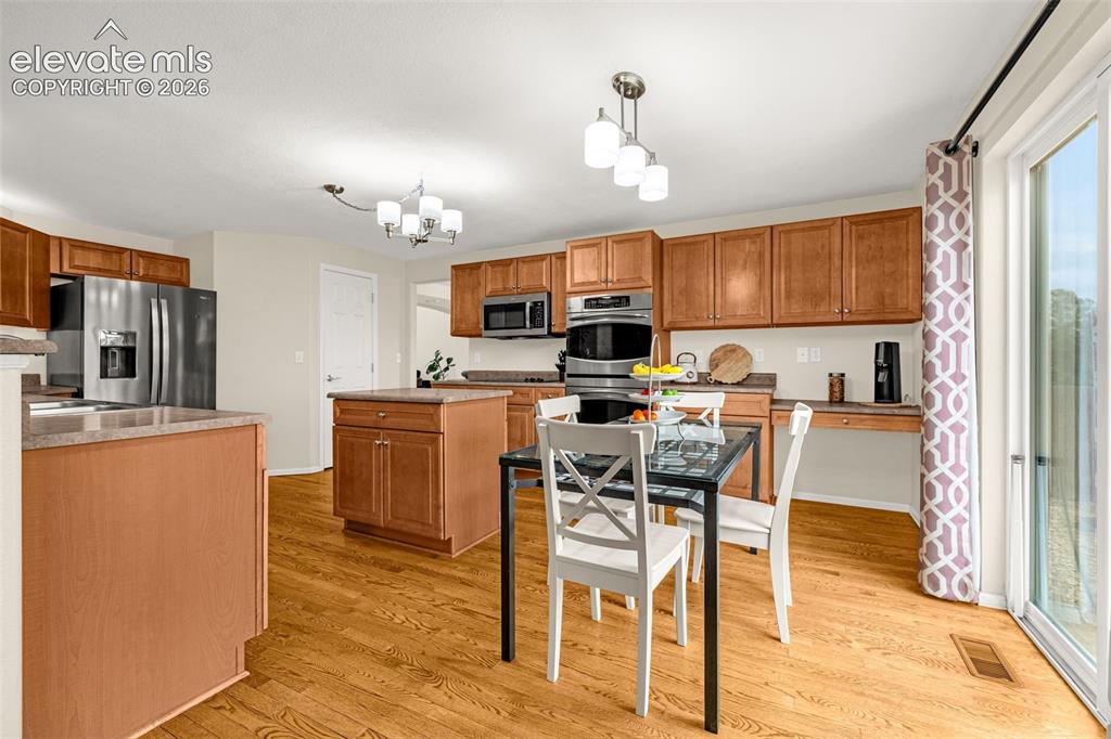 9127 Oakmont Road Peyton, CO 80831 - Photo 9 of 49 a kitchen with stainless steel appliances kitchen island granite countertop a refrigerator a stove top oven a sink dishwasher and white cabinets with wooden floor