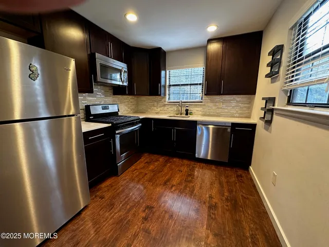 a kitchen with stainless steel appliances granite countertop a refrigerator a sink dishwasher a stove and white countertops with wooden floor