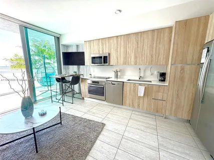 a living room with stainless steel appliances furniture a rug a fireplace and a large window