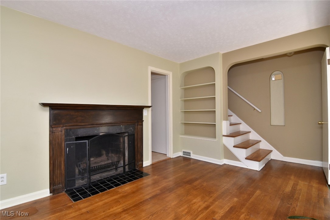 3679 Fenley Road Cleveland Heights, OH 44121 - Photo 7 of 45 Unfurnished living room featuring built in features, stairs, a textured ceiling, a fireplace, and dark wood finished floors