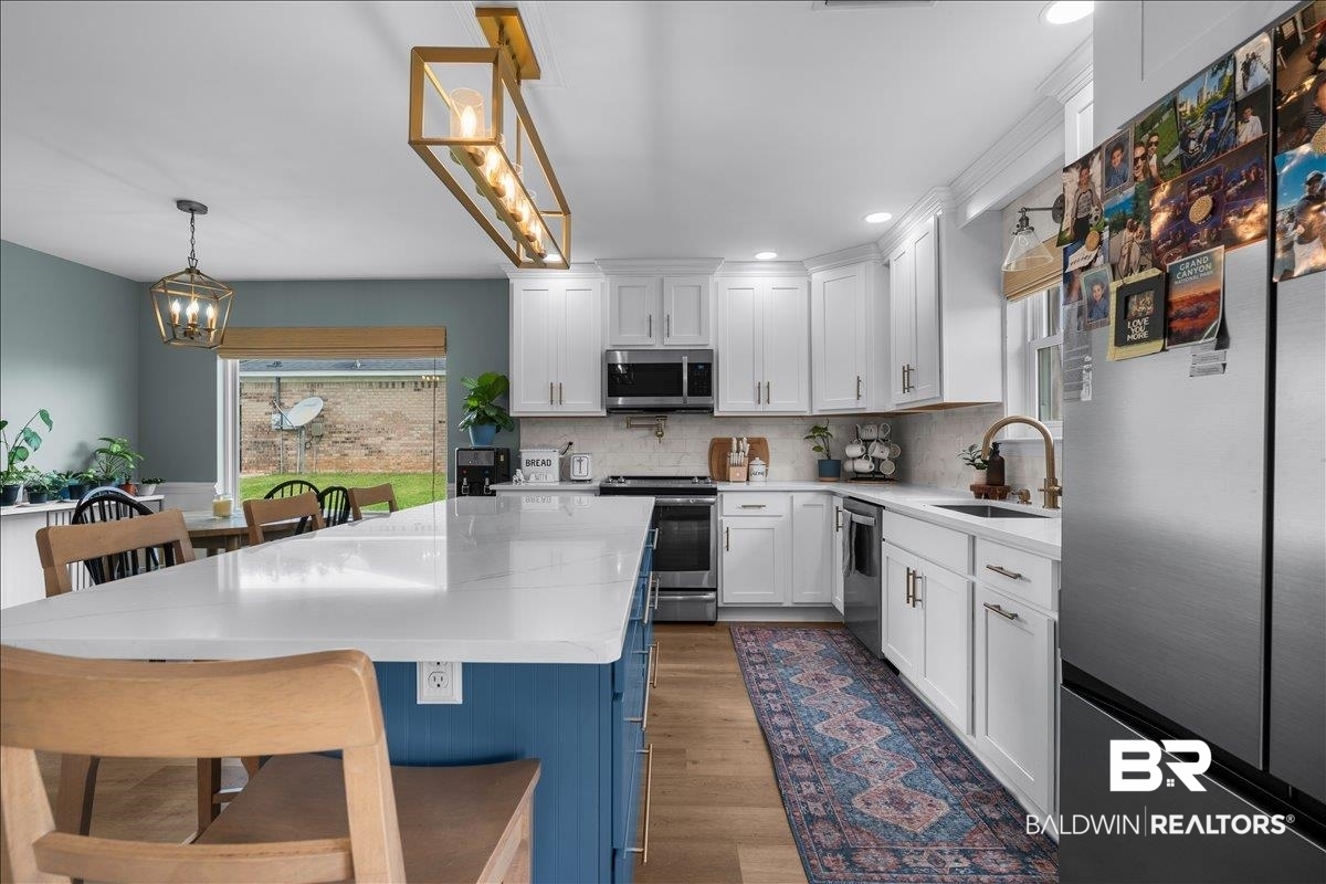 8952 Sherman Road Foley, AL 36535 - Photo 15 of 41 Kitchen featuring a large central island with a white countertop and blue base cabinetry, stainless steel appliances, white perimeter cabinetry, and wood-finish flooring