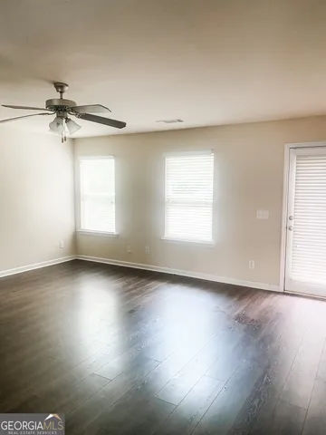 an empty room with wooden floor fan and windows