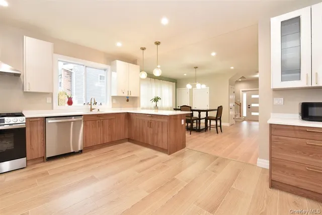 a large white kitchen with a large counter top a sink a window and stainless steel appliances