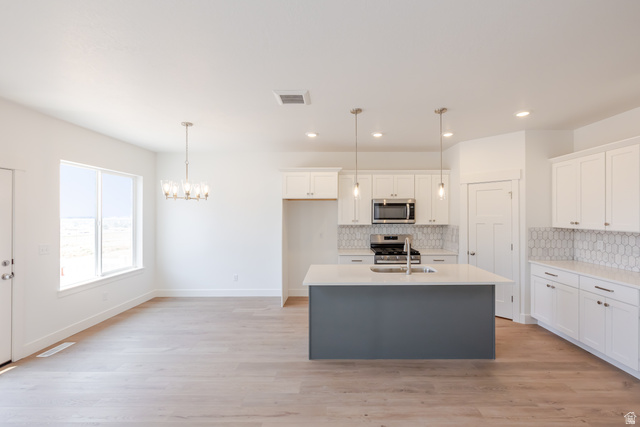 5228 South Acacia Drive, Unit 808 Mapleton, UT 84664 - Photo 6 of 22 Open-concept kitchen and dining area featuring light wood-finish flooring, white cabinetry, stainless steel appliances, a white hexagonal tile backsplash, and a central island with a contrasting dark base and light countertop