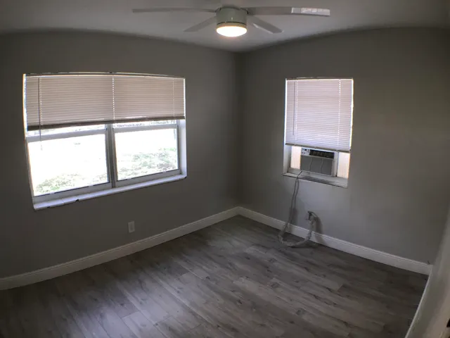 a view of an empty room with wooden floor and a ceiling fan