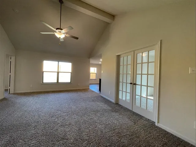 an empty room with chandelier fan and windows
