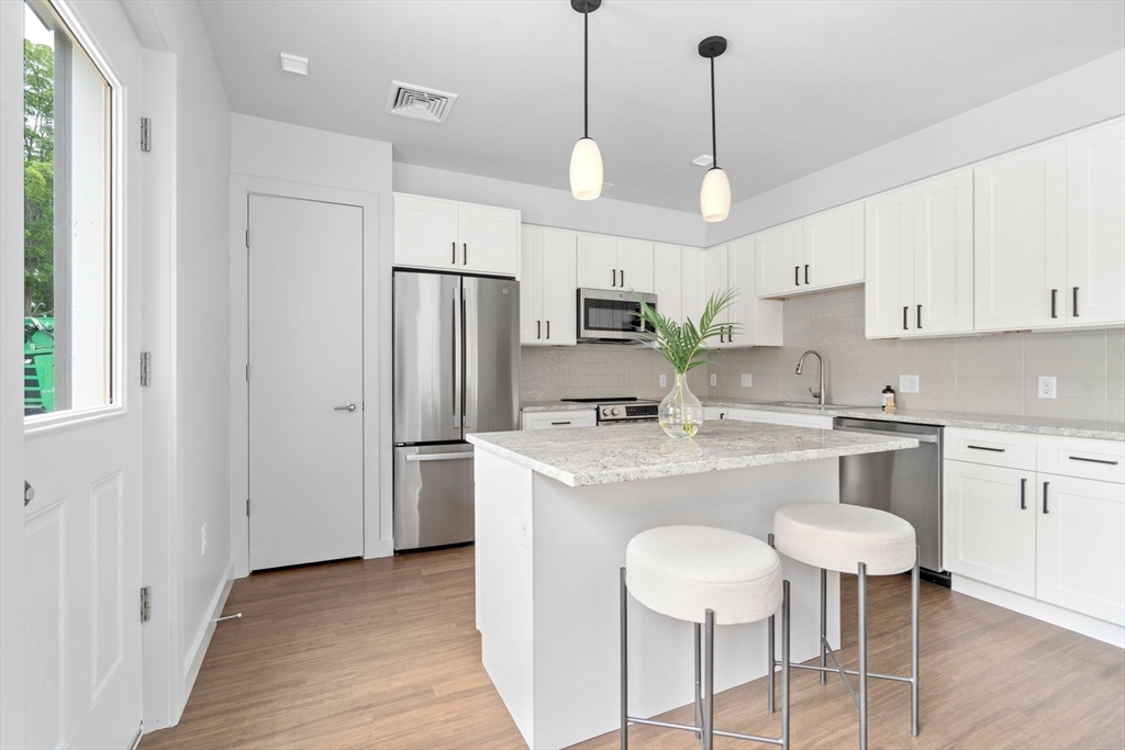 3 B Wilson Street, Unit 3B Natick, MA 01760 - Photo 9 of 33 a kitchen with stainless steel appliances granite countertop a sink a stove a refrigerator and island with wooden floor