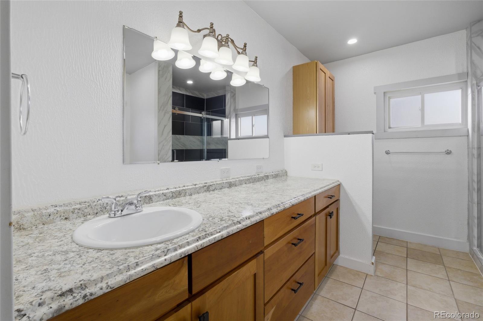 308 Fifth Street Dacono, CO 80514 - Photo 19 of 29 a bathroom with a granite countertop sink a large mirror and a shower