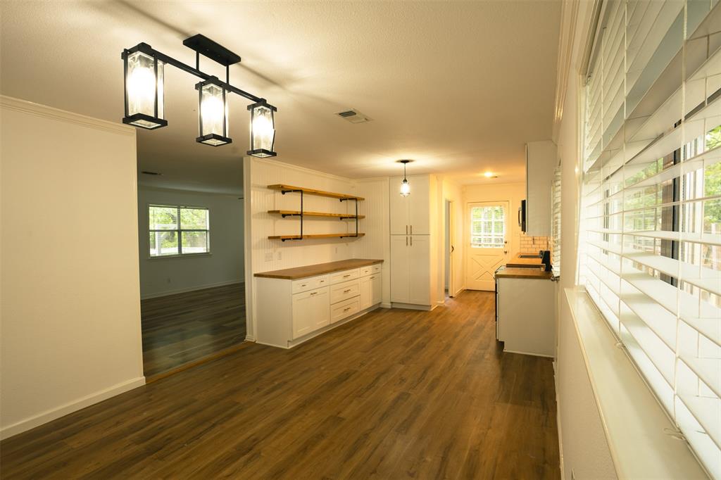 The interior features wood flooring, a white wall with open shelving and white cabinetry, and a modern light fixture