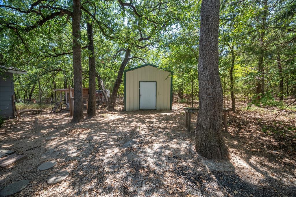 1285 Clark Road Gainesville, TX 76240 - Photo 16 of 20 The property includes a shed with light-colored siding and a white door, surrounded by mature trees providing ample shade