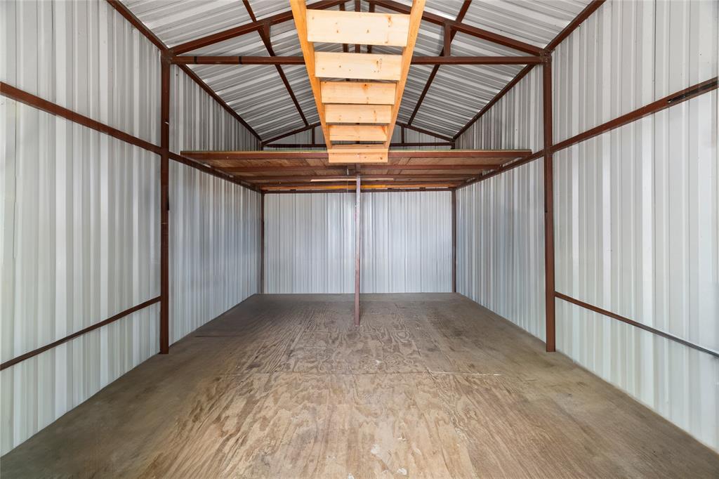 1285 Clark Road Gainesville, TX 76240 - Photo 18 of 20 Spacious interior storage area featuring a wooden floor, metal walls, and a wooden overhead storage platform with a ladder